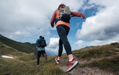 Two hikers in puffy jackets and small backpacks hike swiftly along a ridge-top trail.