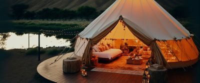 A beautiful dome glamping tent appears lit up at night in a scenic outdoor setting. 