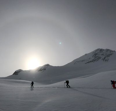 Sun setting over two people skinning in the snow up in the mountains