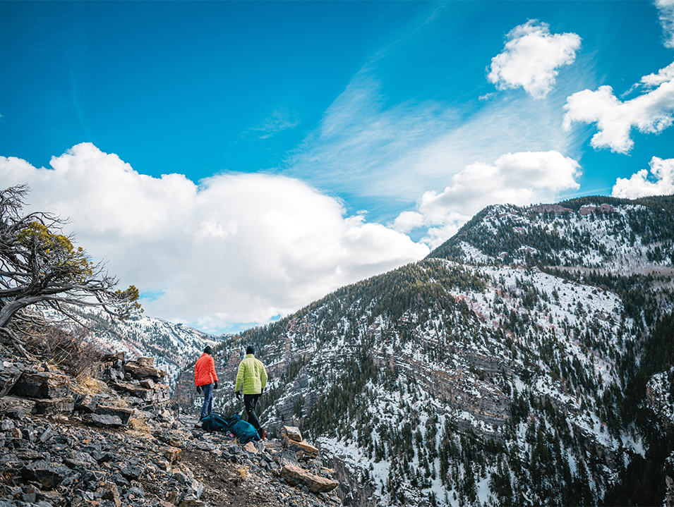 A pair of hikers walk through the mountains on a scenic trail. 
