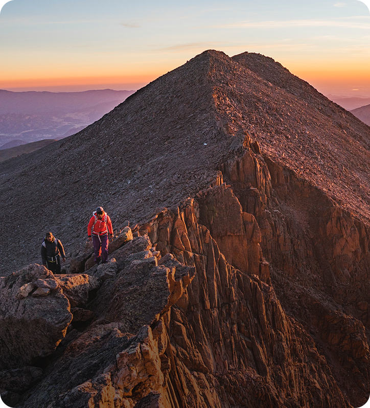 Two alpinists approach the summit at sunrise.