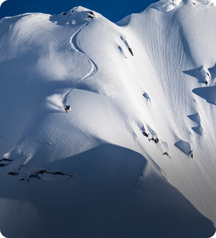 A snowboarder makes his fresh tracks down a beautiful line in the backcountry on a blue bird day.
