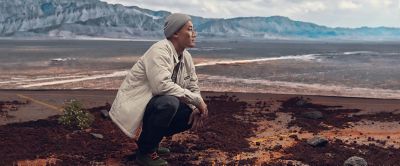 A man crouches down on the ground in a wilderness setting during an overlanding adventure. 