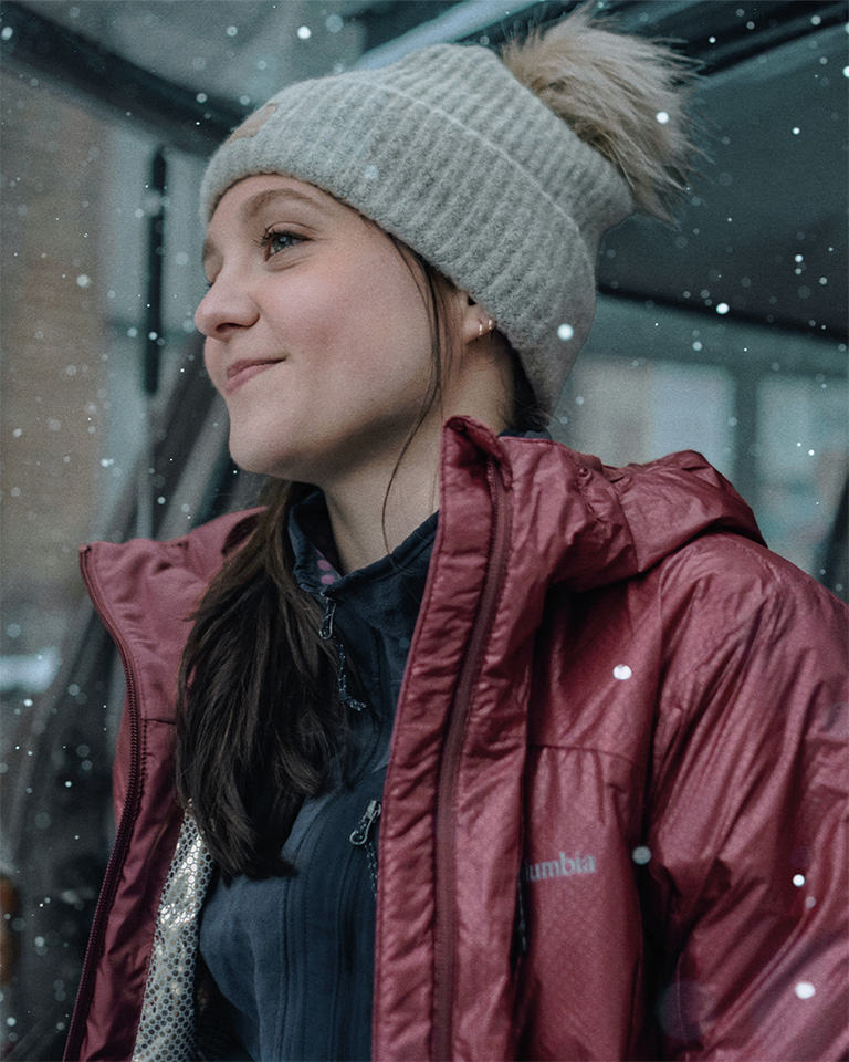 A younger woman in a winter jacket and beanie in the snow.
