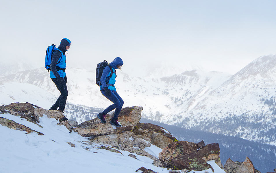 A pair of hikers walks down a snowy mountain on a cold winter day wearing Omni-Heat Infinity jackets. 