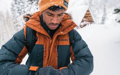 A man tightens the cuff on his parka while standing in deep snow.