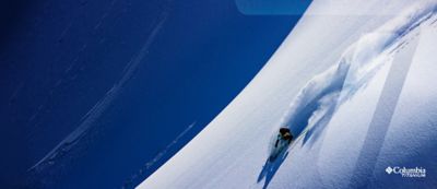 Skier turning down a steep powder slope.