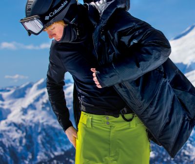Man putting a coat on over a baselayer on the mountain.