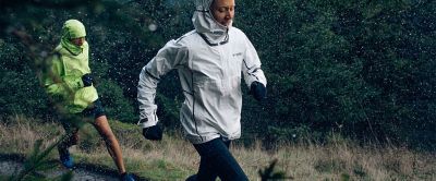 Man and woman running along a forest trail in the rain.