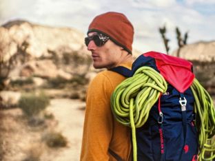 A climber looks back at the camera during his approach, backpack on with rope in toe.