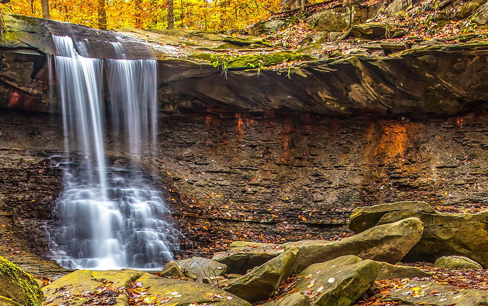 A scenic waterfall plunges over a bed of rocks amid orange and yellow trees at Ohio’s Cuyahoga Valley National Park. 