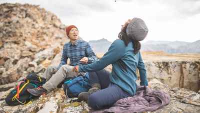Cody tosses a snack for Genevive to catch in her mouth, sitting on their Super/DS™ Stretchdown Hooded Jackets as makeshift blankets while on their hike.