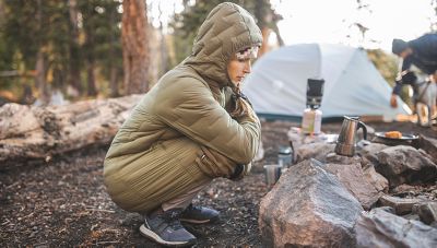 Charlotte is bending down near the fire, completely covered from head to toe by the Super/DS™ Stretchdown Parka.