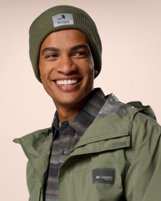A man smiling wearing a green jacket and beanie.