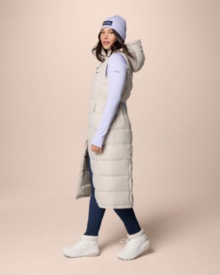 A model wearing a light purple long-sleeve shirt, matching beanie, a long puffer vest, comfy leggings, and winter boots.