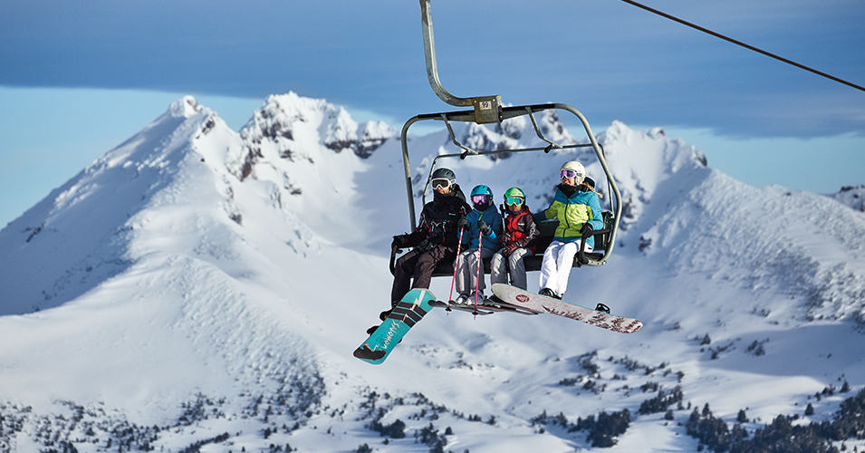 A family of four on the chairlift with a mountain in the background.