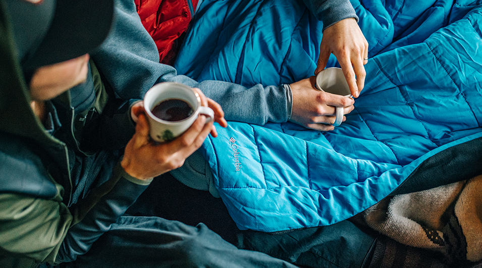 Friends drinking from coffee mugs in blankets.