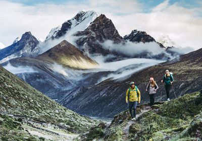 Three hikers trek in Nepal with a beautiful cloudy mountain range in the background, all wearing Ghost Whisperer jackets.