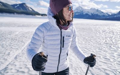 Une femme vêtue d’une doudoune Columbia marche avec des bâtons sur un sol glacé.