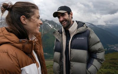 Homme et femme souriants portant des doudounes Columbia sur une colline herbeuse.