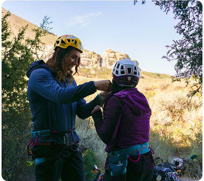 Nikki chatting and laughing with a fellow climber, helping her adjust her helmet