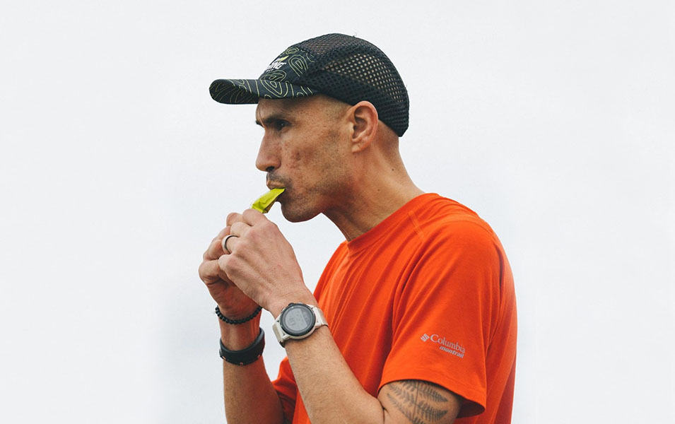 Professional athlete Yassine Diboun wears a red Montrail shirt and black hat as he consumes a Spring Energy pack.
