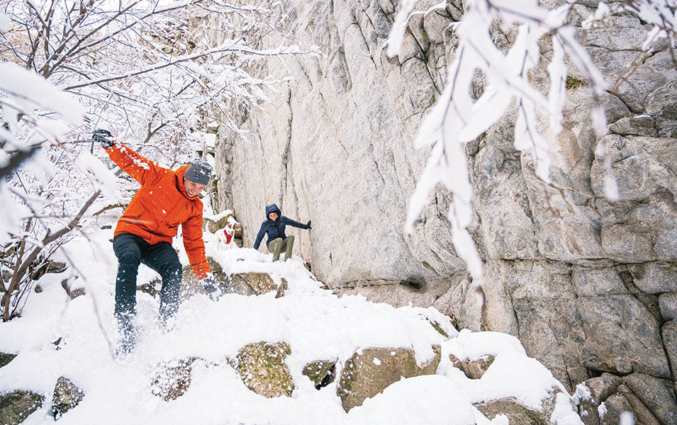 Two people scrambling down a snowy rocky slope. 