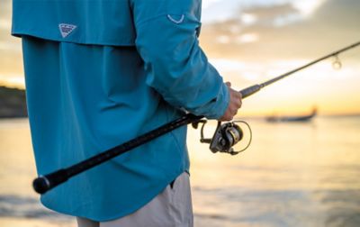 A man wearing a Columbia PFG fishing shirt holds his spinning rod as he gazes out across the water.