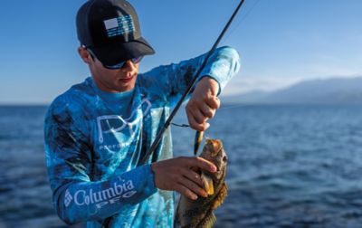 A man with a Columbia PFG sun shirt carefully removes a hook from a fish's gills.