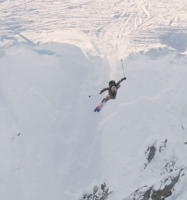 Lily free skiing off a partially snowy rockface.