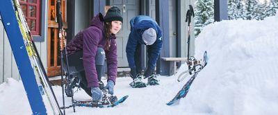 A woman and a man gearing up to go snowshoeing. 