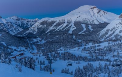 a snowy ski lodge and chairlift with a mountain in the background. 