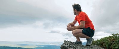 Man perched on rock outcropping looking out. 