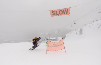 Skiing right by a SLOW sign at a ski resort.