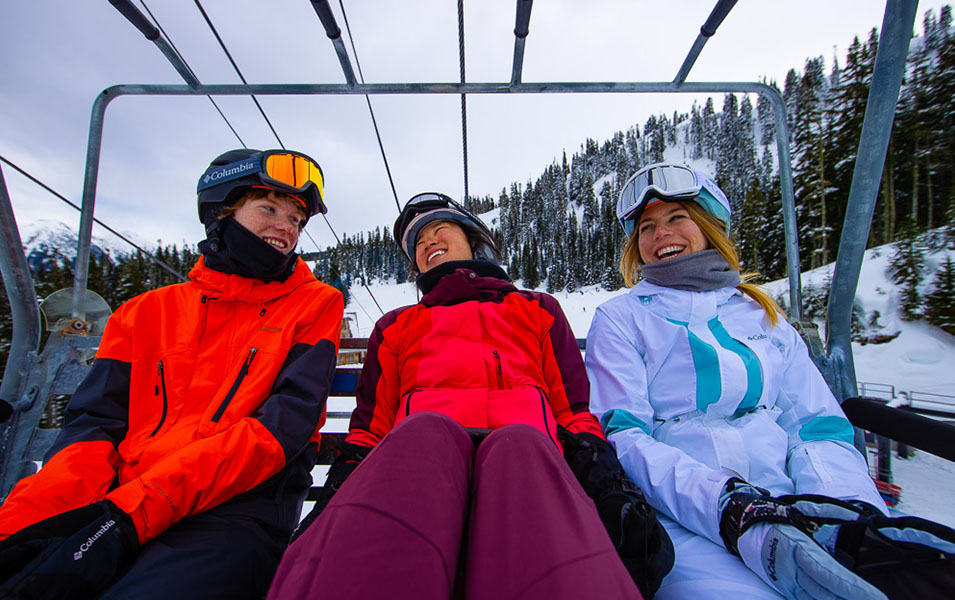 Three skiers ride a chairlift laughing and enjoying themselves on a beautiful winter day.  