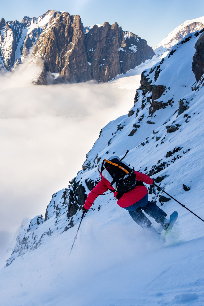 Rachael Burks free skiing off a partially snowy rockface.