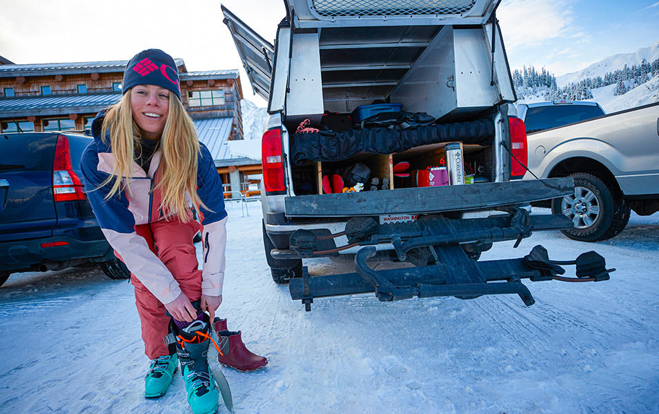 A skier adjusts her boots while smiling at the camera. 