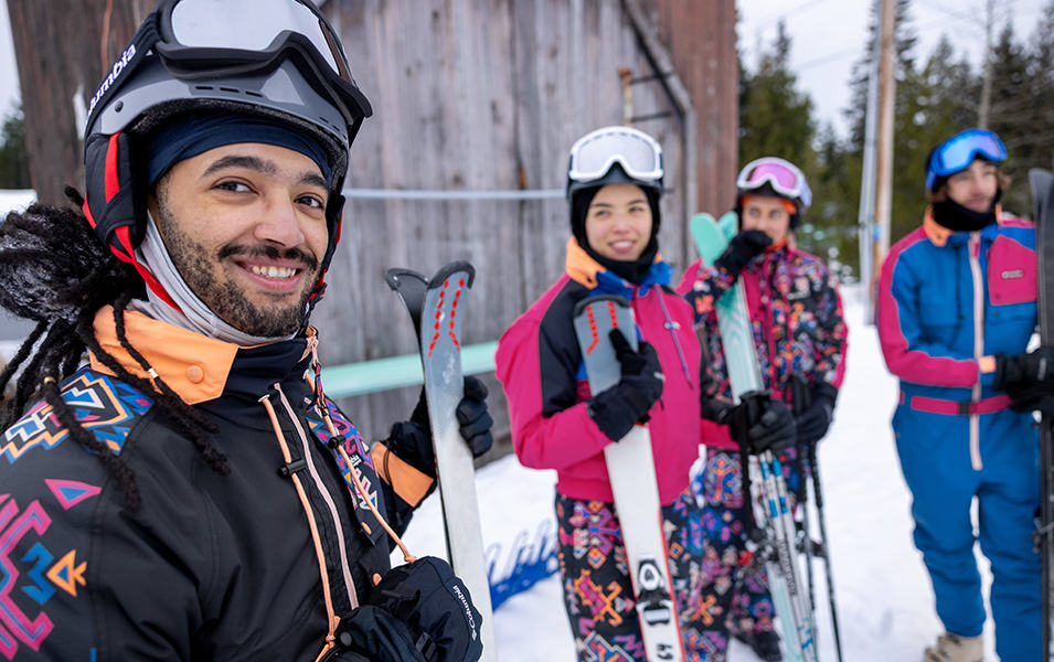 A group of skiers stands on the mountain smiling at the camera.