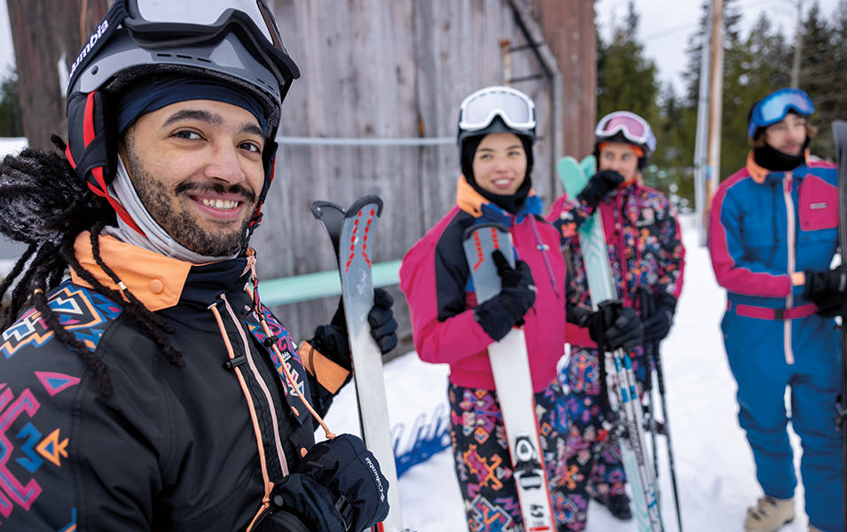 A skier looks at the camera smiling while a gorup of friends stands in the background. 