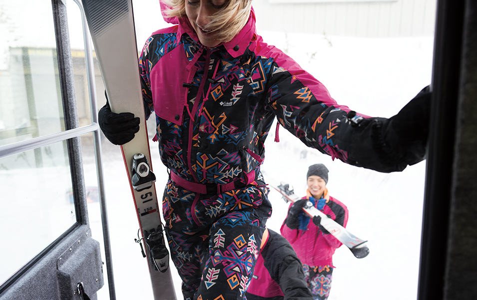 A woman in a pink retro ski suit walks onto the gondola. 