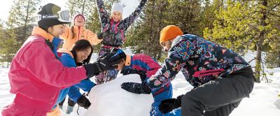 A group of skiers laughs together as they builds a snowman.