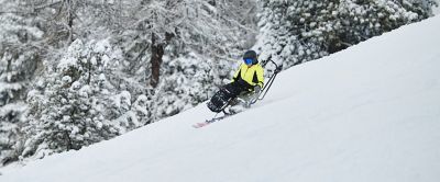 A person using adaptive ski equipment navigates down a snow-covered slope, surrounded by a post-card perfect winter landscape.