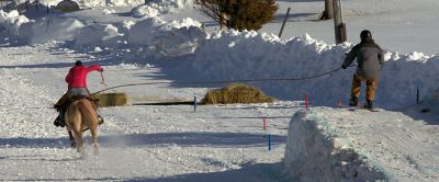 A rider and horse tow a person on skis over a snow-covered jump.