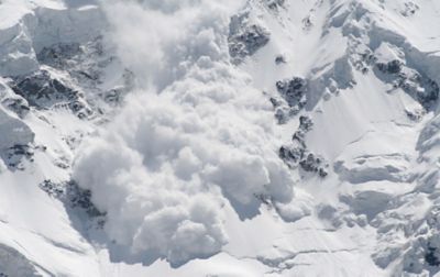 Snow cascades down a steep, glaciated face, swallowing everything in its path. 