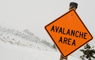 An orange warning sign marks the avalanche zone, with fencing in the background keeping the drifting snow from blocking the road.  