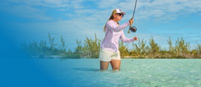 A woman fishing in shallow water casting her line.