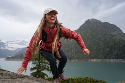 Hiker scrambles up a rocky trail in a serene mountain landscape.