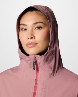 A woman wearing a pink rain jacket with the hood up.