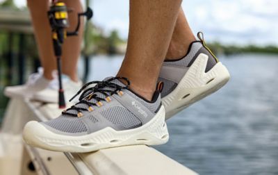 A person wearing Columbia PFG shoes with biomimicry-inspired soles maintains a steady balance on the slippery rail of a fishing boat.
