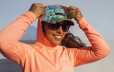 A smiling woman tugs the hood of her sun sun shirt over her PFG ball cap.